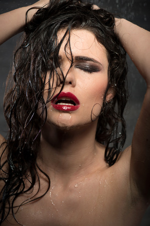 Half-length portrait of beautiful sexy dark-haired woman with great evening make up standing with closed eyes under the rainの写真素材