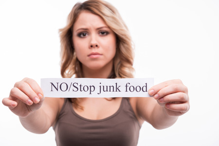 Closeup portrait of young attractive unhappy blonde woman with card isolated on white background. No stop junk foodの写真素材