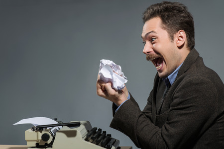 Waiting for idea.  Young author screaming from anger while sitting at his working place against grey backgroundの写真素材