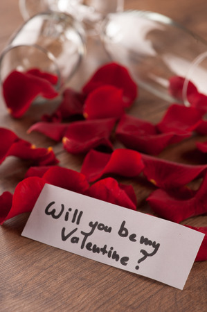 Happy day. Closeup image of composition with champagne glasses decorated with rose petals and greeting card to Saint Valentines Day placed on wooden backgroundの写真素材