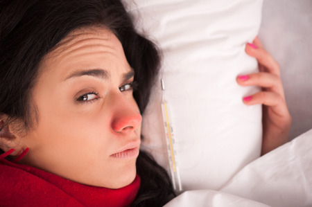 Take a sick day. Closeup image of young sick woman lying in bed with sore throat in scarf and...