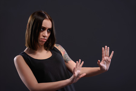 Terrified young woman looking at somebody and stretching out hand while standing against black backgroundの写真素材