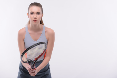 Ready to win. Beautiful young woman in sports clothes holding tennis racket and looking at camera while standing against white backgroundの写真素材