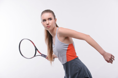 Ready to serve. Beautiful young woman in sports clothes holding tennis racket and looking away while standing against white backgroundの写真素材