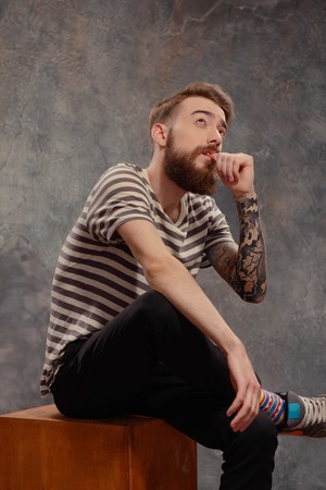 Independent thinker.  Portrait of young bearded tattooed man in a striped longsleeve looking up in a...