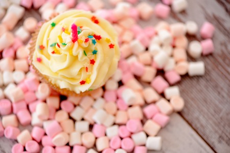 Waiting for birthday party. Top view image of cupcake with a birthday candle surrounded by marshmallow on wooden tableの写真素材