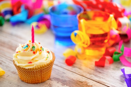 Celebrating a special day. Side view image of a cupcake with multicolored confetti as a frame and bright glasses on the backgroundの写真素材