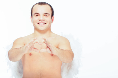 Angel in love. Portrait of an adorable little cupid showing with his fingers a heart and smiling at...