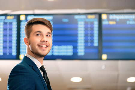 Just in time for check-in. Low angle image of a handsome businessman wearing  suit smiling away while standing against flights schedule in the airportの写真素材