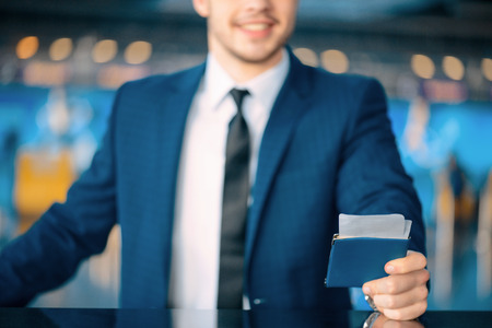 Ready for check-in. Cropped image of a handsome young businessman in suit stretching out his ticket while standing in front of the airline check in counter in the airportの写真素材