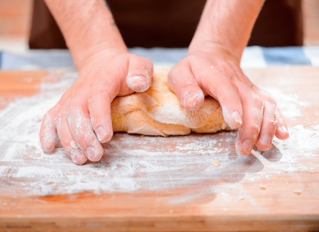 Kneading the dough. Closeup of male baker kneading the dough on the wooden cutting board