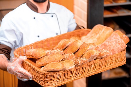 Proud of his baked goods. Cropped image of a handsome young man in apron holding basket with baked goods in bakery shopの写真素材