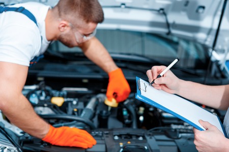Running diagnostics. Two handsome car mechanics in uniform checking the engine under hood in the car service station and checking in service orderの写真素材