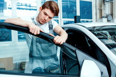 Double- check the door. Portrait of a concentrated handsome mechanic in uniform checking the door of the car at auto service stationの写真素材