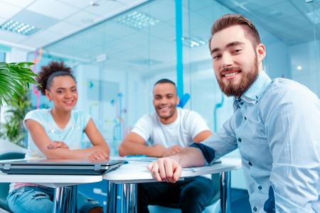 Join our creative team. Low angle portrait of beautiful young people sitting at the table and smiling at camera in creative spaceの写真素材