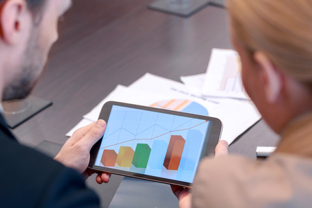 Trend of stable growth. Female and male business partners look at a screen of the tablet device where they see diagram in selective focusの写真素材