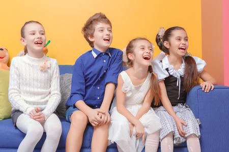 Laughing out loud. Cute school children laughing loudly when sitting on the sofa at kids roomの写真素材