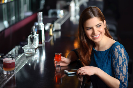 Have fun. Young beautiful woman laughing when using phone by the bar counterの写真素材