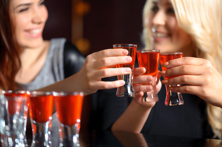 Friendship forever. Selective focus on three shots with red beverage and smiling girls in blurry holding glassesの写真素材