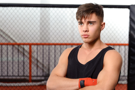 Fighter. Portrait of a young boxer standing in a fighting cage in a gymの写真素材