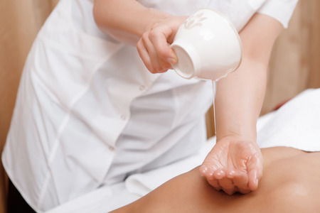 Massage oil. Close-up of masseur hands pouring massage oil on the back of a female clientの写真素材