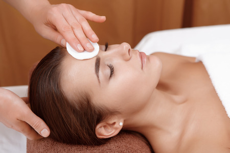 Perfect clean. Close-up of a female cosmetologist cleansing with sponge face of a female client of beauty salonの写真素材