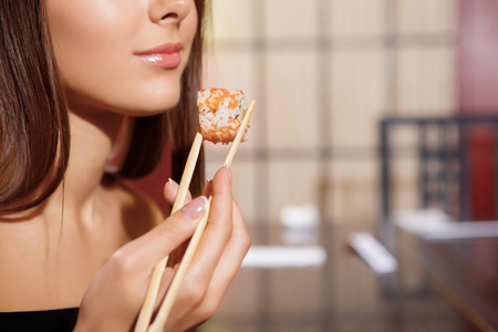 Japanese cuisine. Cropped view of a young beautiful woman holding with chopsticks a rollの写真素材