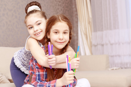 Lets hug. Two cute girls sitting at table hugging and writing.の写真素材