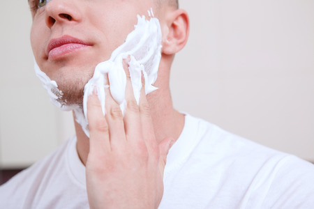 Spread over. Handsome young guy standing in front of mirror and spreading over shaving gel.