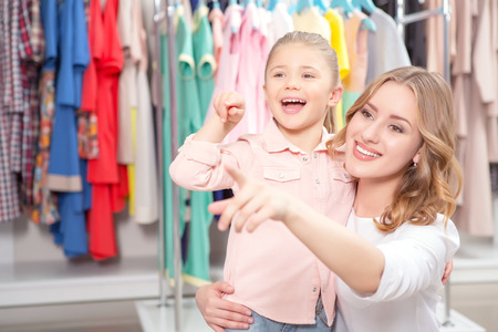 Shopping. Young mother sitting in a fashion store holding her small smiling daughter and pointing somewhereの写真素材