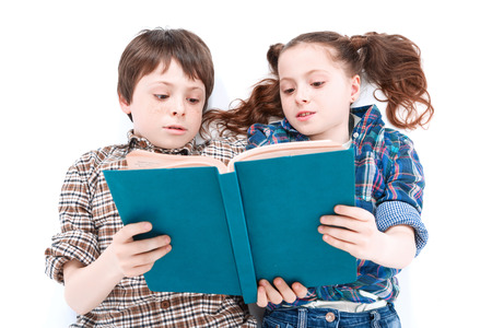 Portrait of a small handsome boy lying on the floor on his back and his small sister lying next to him reading a blue book top view, isolated on white backgroundの写真素材