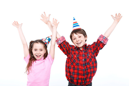 Party time. Small handsome boy and his little pretty sister wearing cone caps smiling and holding their hands up looking happy, isolated on white backgroundの写真素材