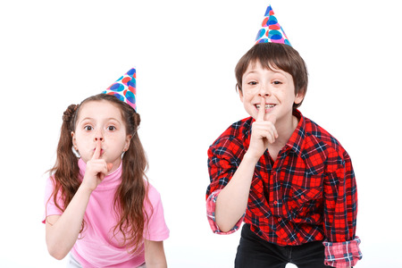 Tss. Small handsome boy and his little pretty sister wearing cone caps holding their fingers near mouth showing to be silent  isolated on white backgroundの写真素材