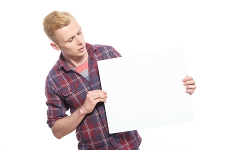 Interesting thing. Attractive young man looking at white sheet of paper that he is holding on...