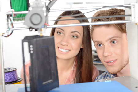 Young beautiful student smiling and her handsome colleague watching happily the black item making by...