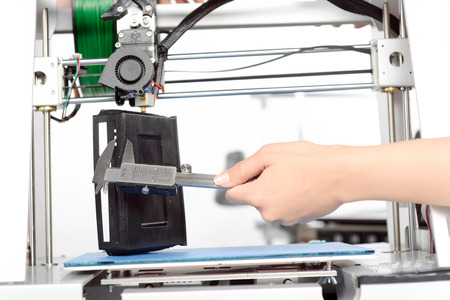Close up of a hand holding calipers and measuring a black item while printing it on 3D-printer