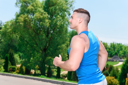 Portrait of a young handsome muscular sportsman running and smiling, wearing white and blue...