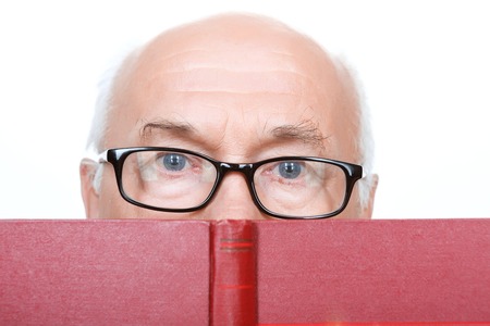 Involved in reading. Wise grandfather in glasses holding the book near his face and looking straight...