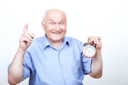 Refreshing morning. Brisk grandfather  holding the alarm clock and pointing his index finger up while expressing joy.の写真素材