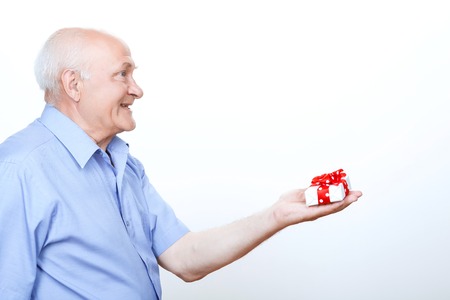 Congratulate you. Upbeat grandfather bending his arm and holding the present on it while standing isolated on  white background.の写真素材