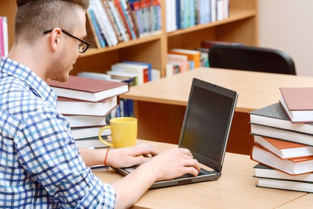Portrait of a handsome smart student wearing glasses and blue checkered shirt sitting at the table...