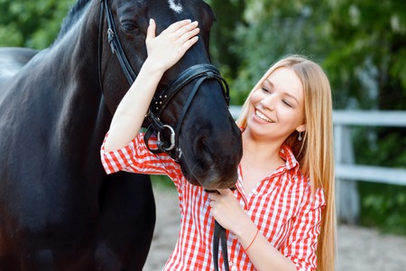 Best friends. Positive girl palming the horse and keeping her glance down while standing behind the...