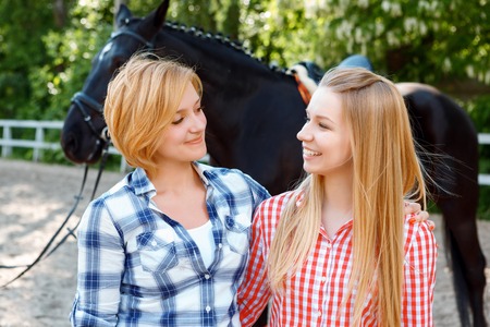 Dear sister. Upbeat sisters embracing and looking at each other with the horse standing in the background.の写真素材