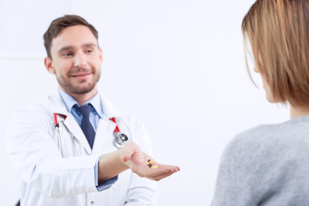 Helpful hand. Nice doctor giving pills to  patient while sitting at the table and talking to her.の写真素材