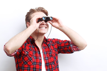 Look up. Pleasant guy holding binoculars with his hands and  looking through it up.