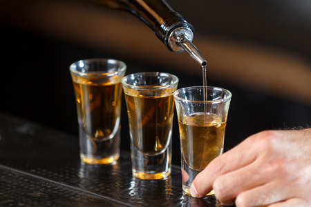 Close up photo of hands of a bartender pouring some drink into shot glasses on a wooden counterの写真素材
