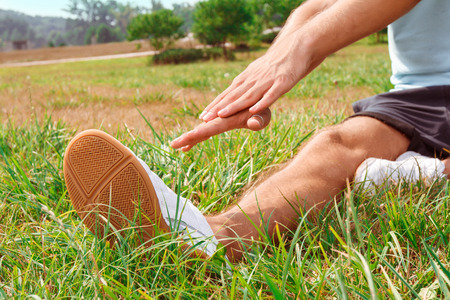 Selective focus of foot of the sportsman sitting on grass and doing sport activities.