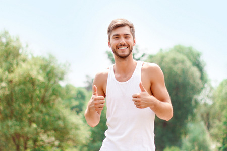 Upbeat smiling young man holding hand raised and thumbing up while evincing positivity.の写真素材