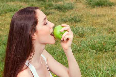 Close up pleasant young girl holding apple and eating it.の写真素材