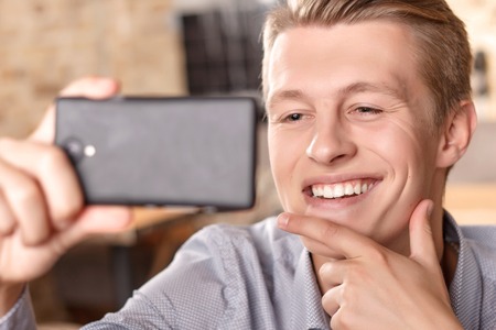 Im so fancy. Handsome smiling man touching his chin with fingers and doing selfieの写真素材